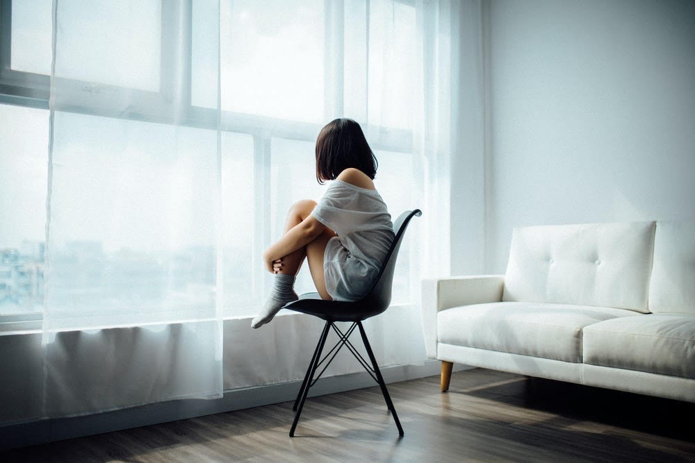 A woman sitting on a chair in front of a window.