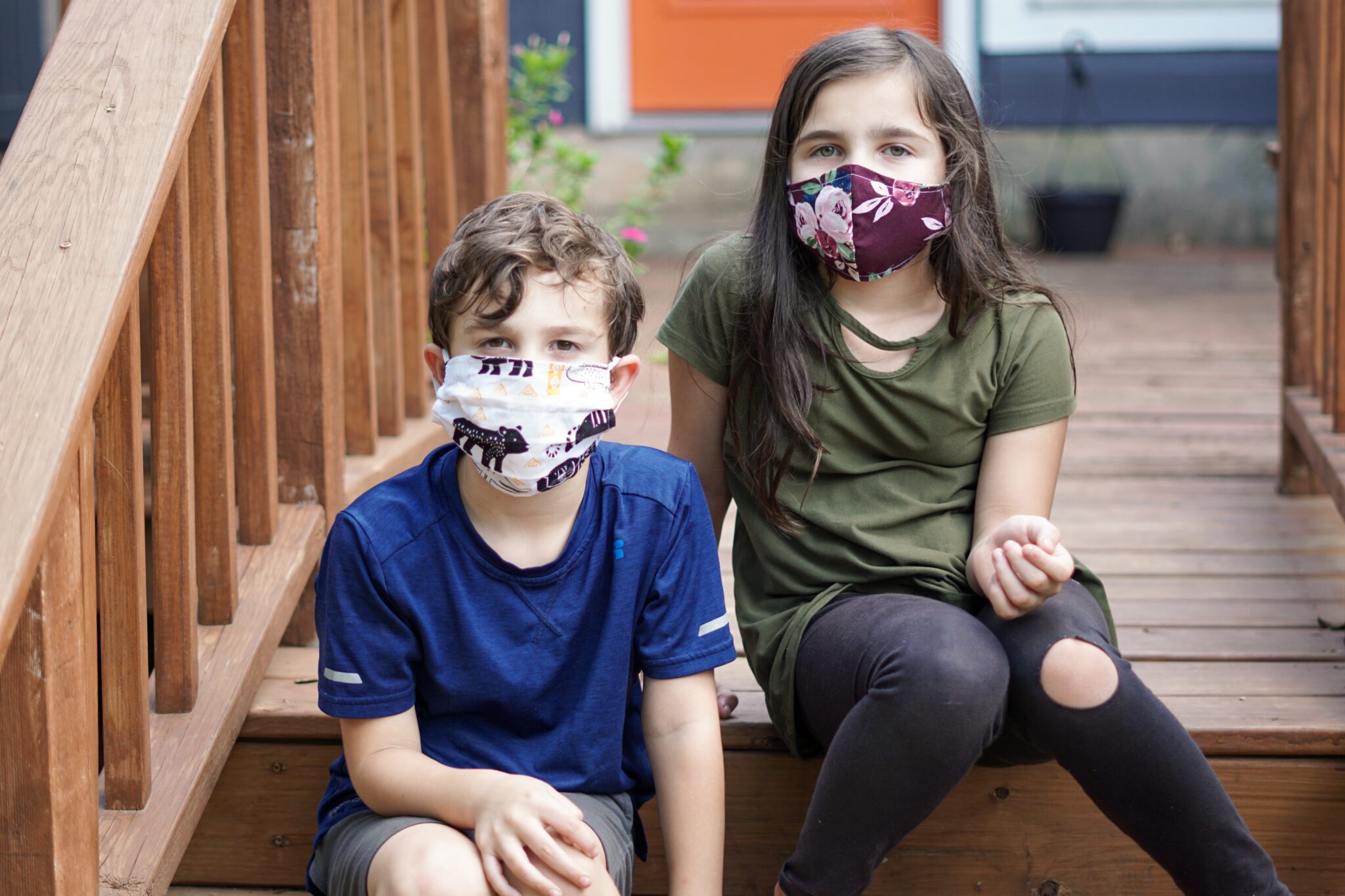 Two children sitting on steps wearing face masks to protect their mental health.