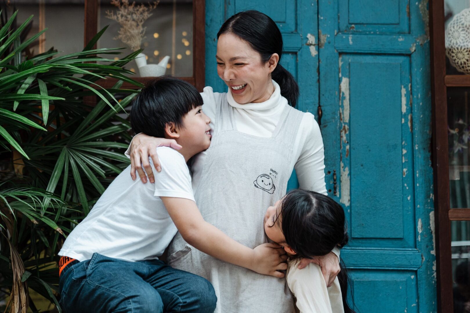 A woman is hugging her children in front of a blue door, emphasizing the importance of children's mental health.