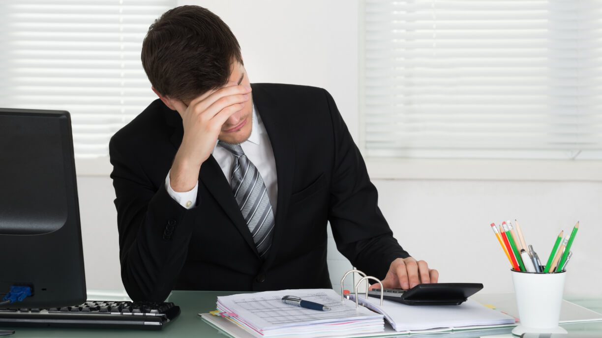 A man in a suit sitting at a desk with management software on a calculator.