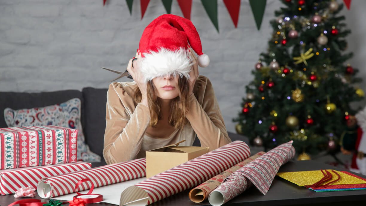 A woman in a santa hat sitting at a table with christmas presents, organizing them using management software.
