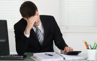 A man in a suit sitting at a desk with management software on a calculator.