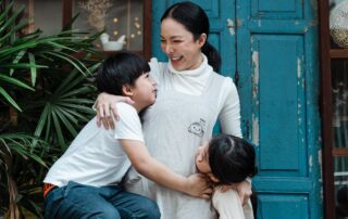 A woman is hugging her children in front of a blue door, emphasizing the importance of children's mental health.